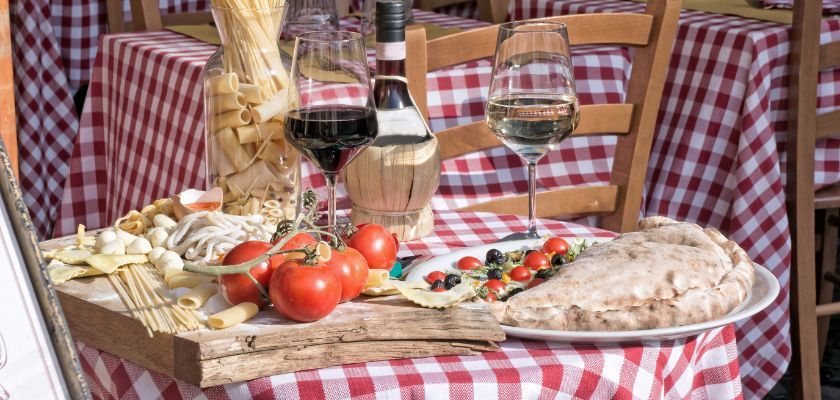 Prikaz tradicionalnog jela u konobi s posluženim domaćim vinom. Na stalu se nalazi vino stara butelja, čaše, rajčice, tijestenina, kruh pečen u krušnoj peči. posluženo na izrezbarenom komadu drveta.